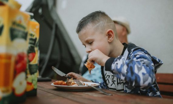 Young boy savoring a grilled chicken meal during an outdoor barbecue.
