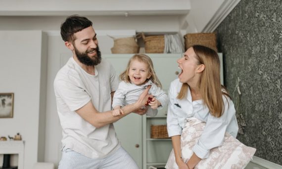 Joyful parents playing with their daughter at home, showcasing love and happiness.