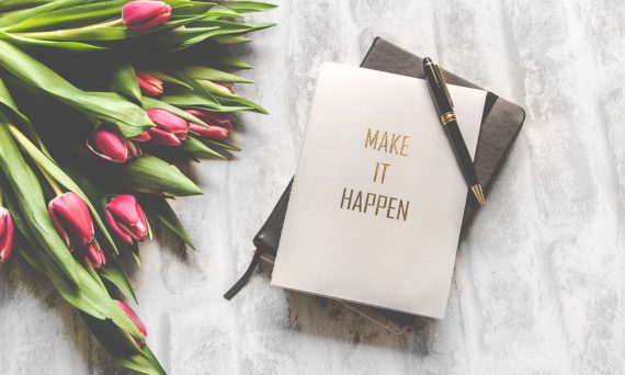 A notebook with 'Make It Happen' inscription beside a bouquet of pink tulips, capturing inspiration.